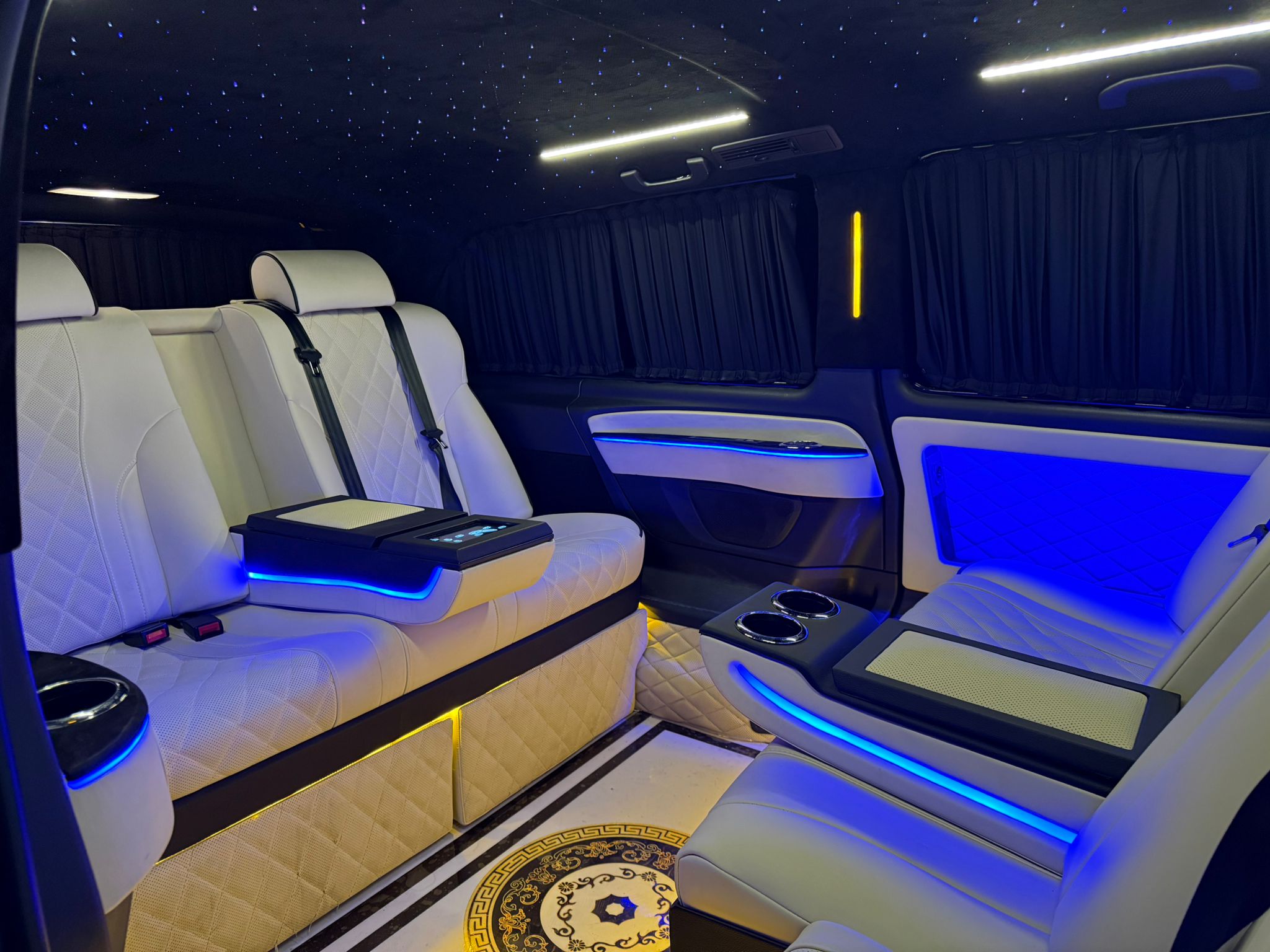 Intérieur Mercedes V-Class Lounge — banquette et fauteuil pivotant cuir blanc, LED bleues ambiance, motif sol design